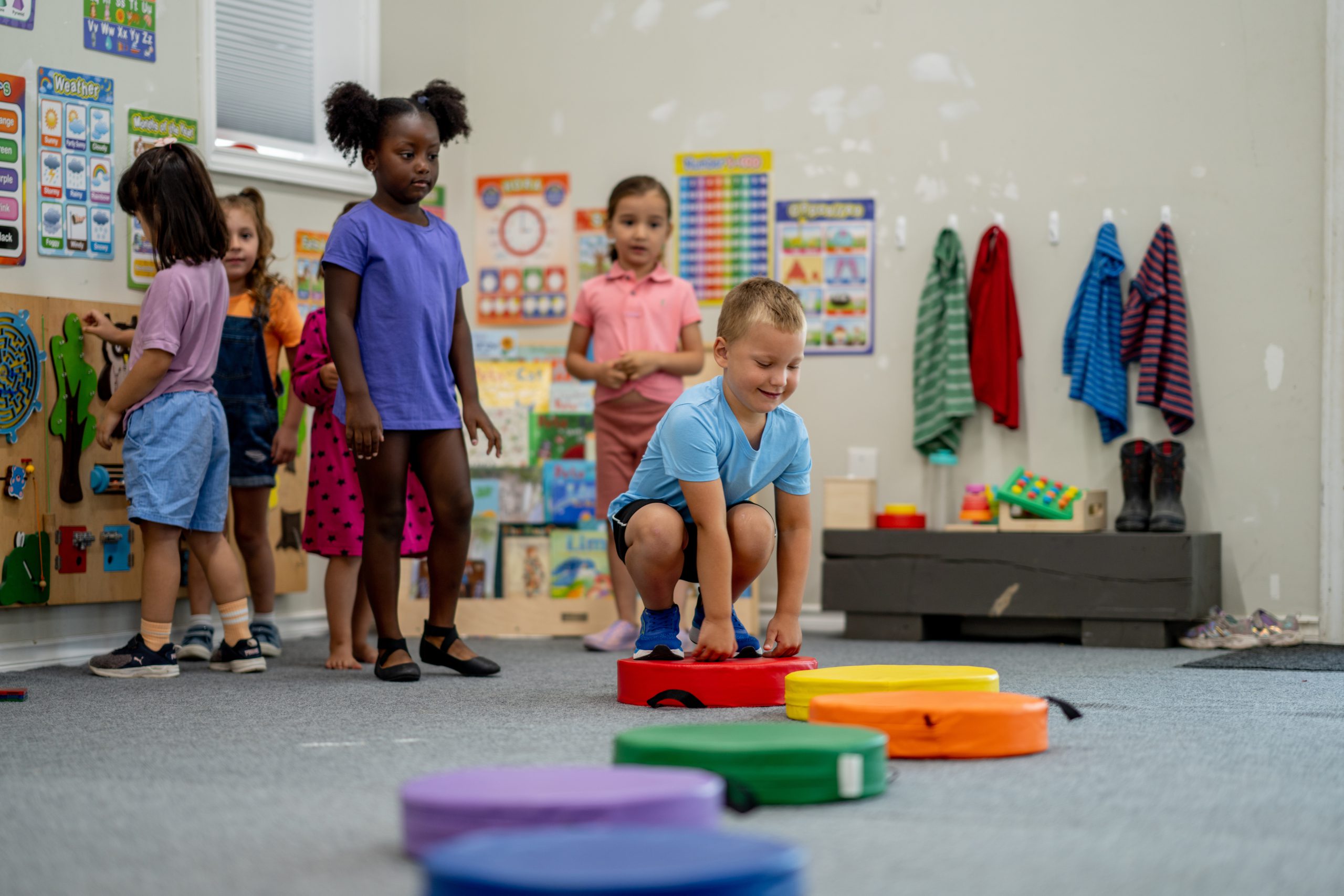 Des enfants participent à un atelier de psychomotricité avec des blocs d'équilibre colorés.